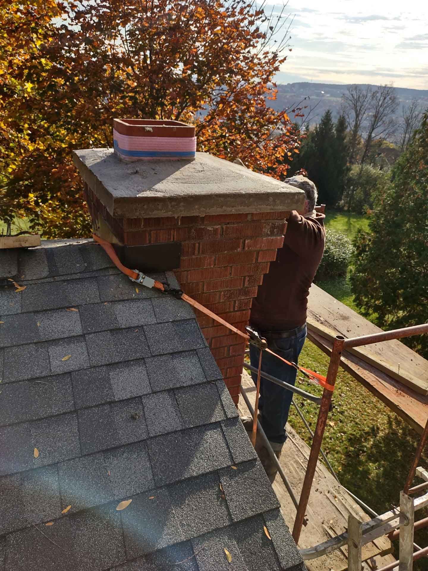 A man is standing on top of a roof next to a chimney.