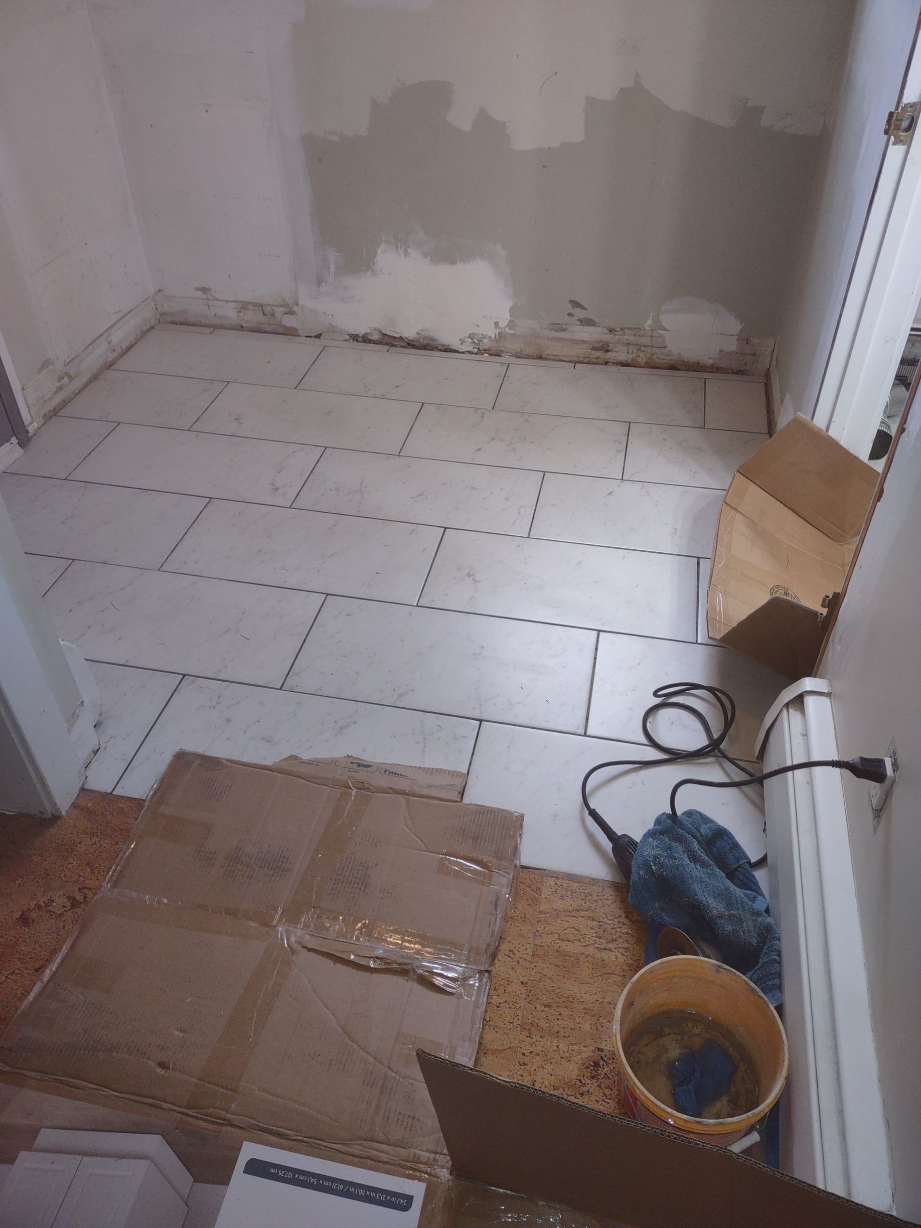 A room with a bucket of water and a drill on the floor.