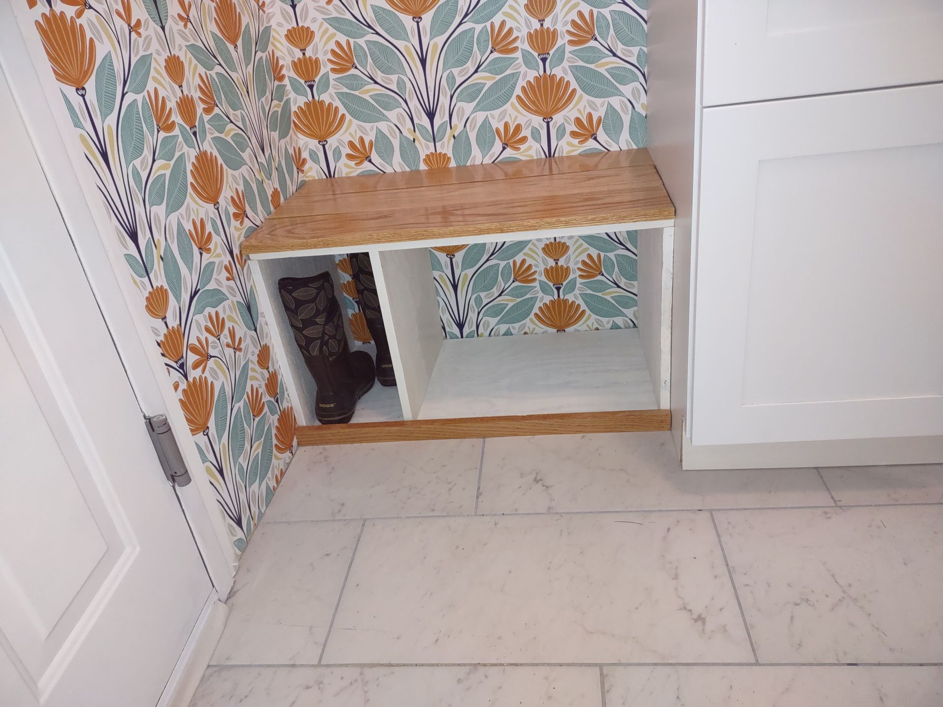 A corner of a room with a shelf and a floral wallpaper.