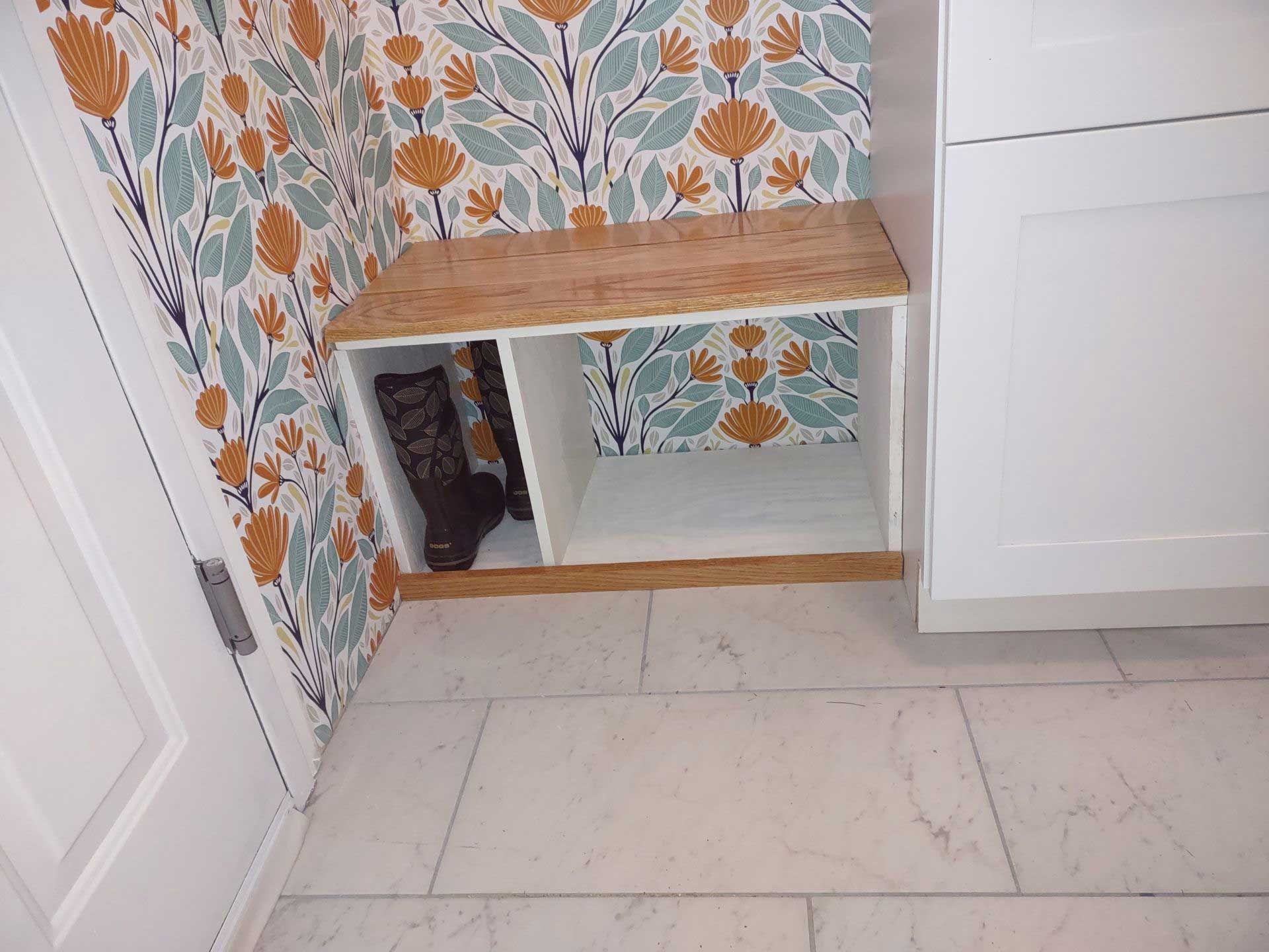 A corner of a room with a shelf and a floral wallpaper.