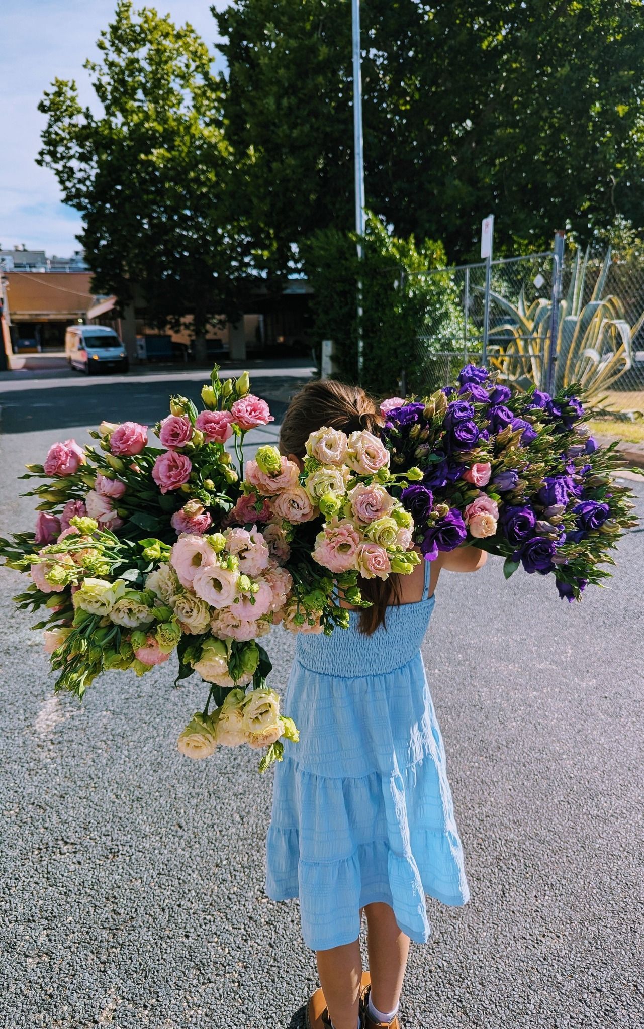 A Little Girl in a Blue Dress is Carrying a Large Bouquet of Flowers — Hello Poppy Lane Florist In Albury, NSW
