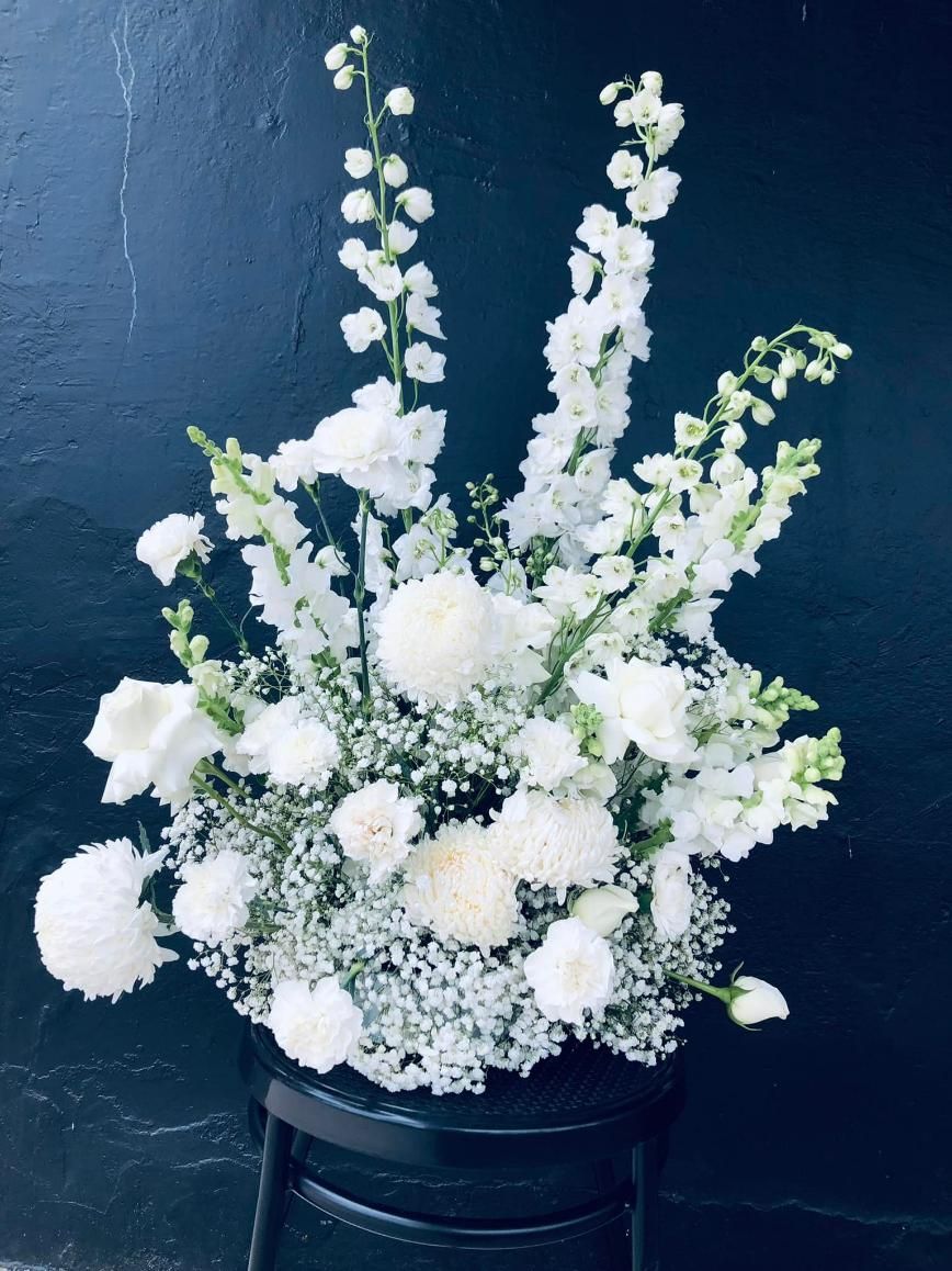 A Vase Filled With White Flowers is Sitting on a Black Chair — Hello Poppy Lane Florist In Wodonga, VIC