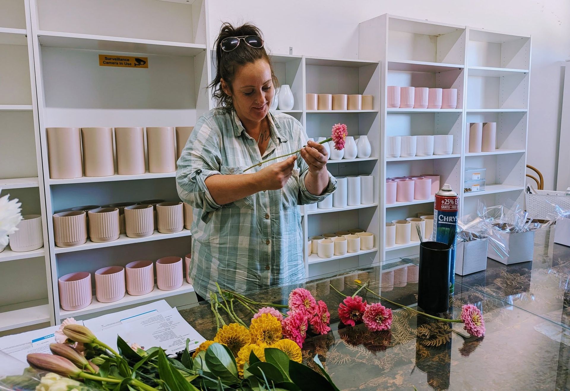 A Woman is Sitting at a Table With Flowers in Front of Shelves — Hello Poppy Lane Florist In Albury, NSW