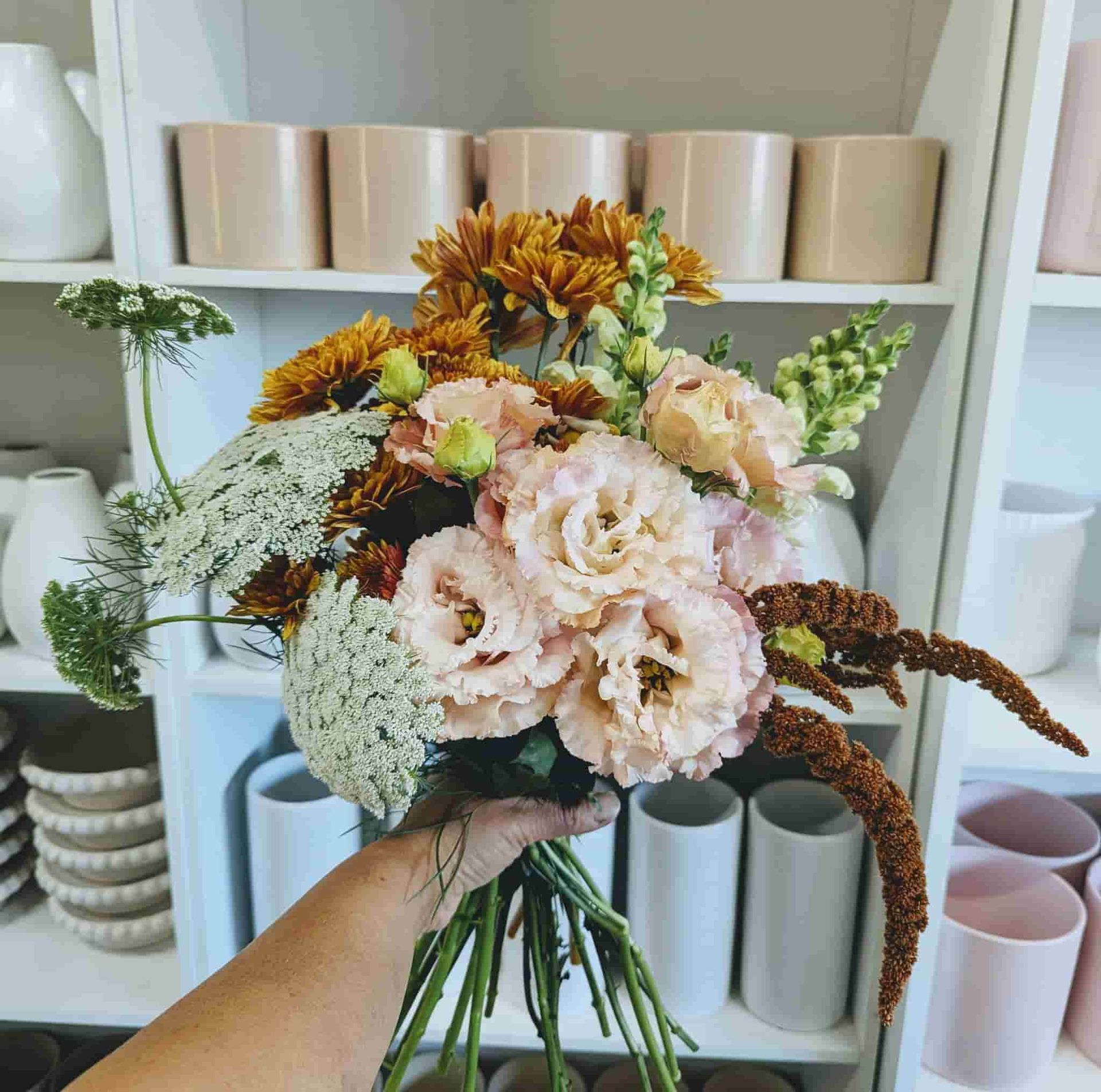 A Person is Holding a Bouquet of Flowers in Front of a Shelf Full of Vases — Hello Poppy Lane Florist In Rutherglen, NSW
