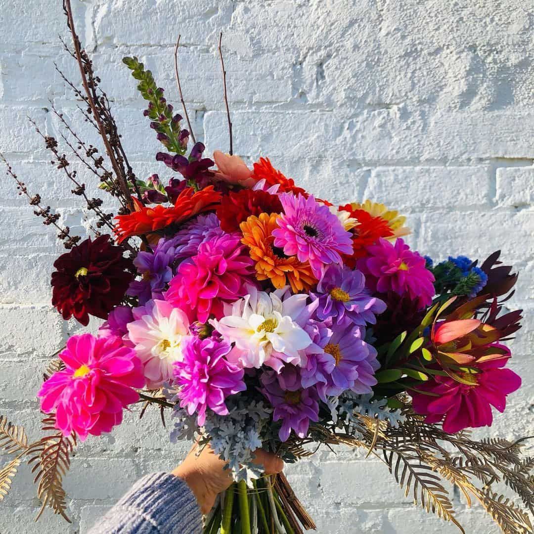 A Person Is Holding a Bouquet of Flowers in Front of A White Brick Wall — Hello Poppy Lane Florist In Ebden, VIC