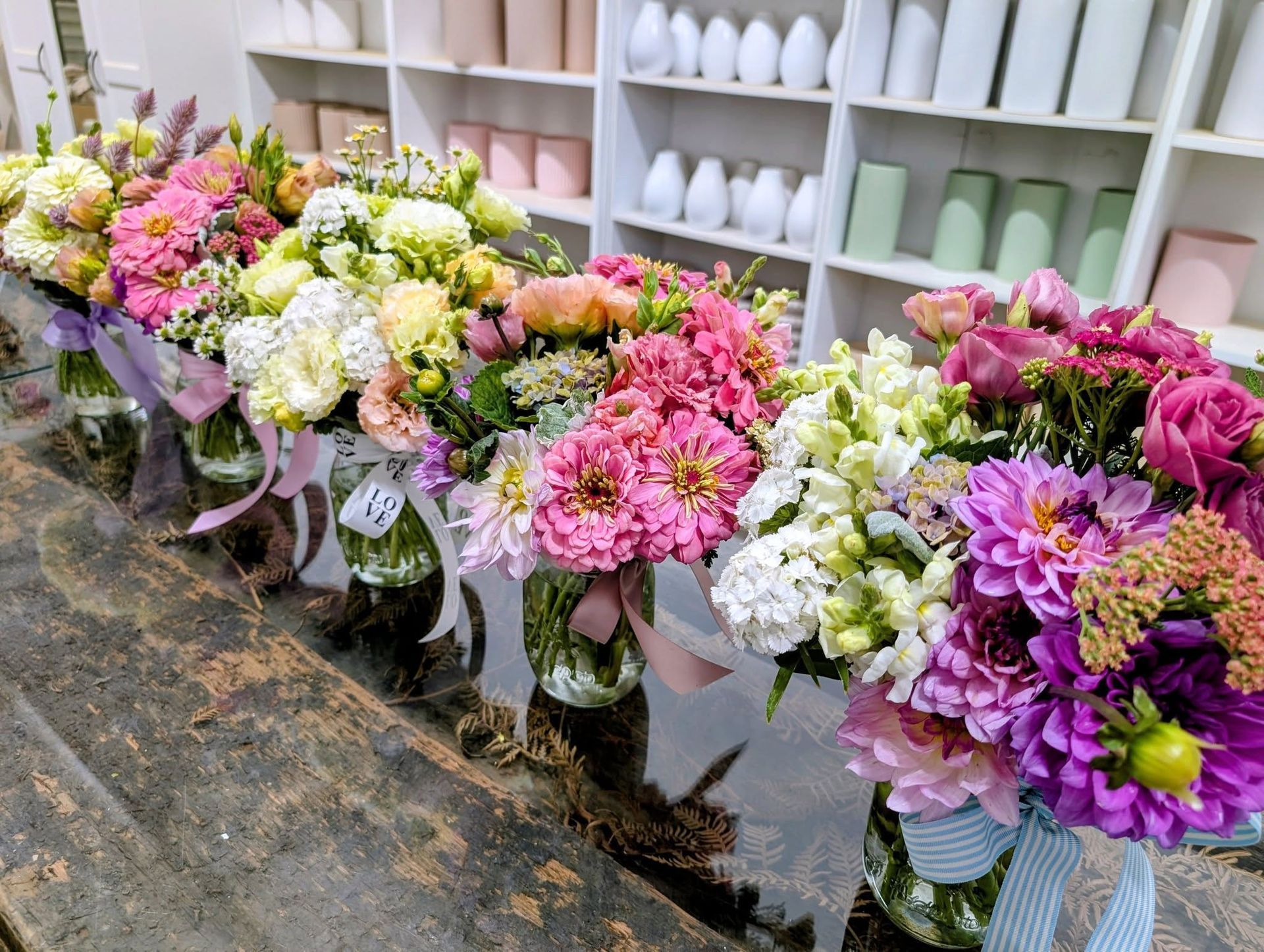 Colourful flower arrangements in mason jars on a wooden table, store setting — Hello Poppy Lane Florist In Albury, NSW