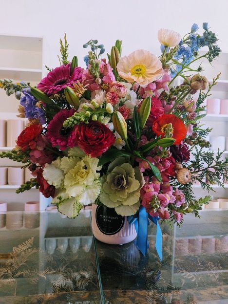 Colourful Flower Arrangement in a Pink Vase Tied With Blue Ribbon, Set on a Glass Surface — Hello Poppy Lane Florist In Albury, NSW