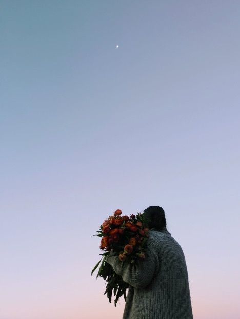 Person Carrying a Large Bouquet of Orange Flowers Against a Pastel Pink and Blue Sky, With a Single White Dot in the Sky — Hello Poppy Lane Florist In Albury, NSW