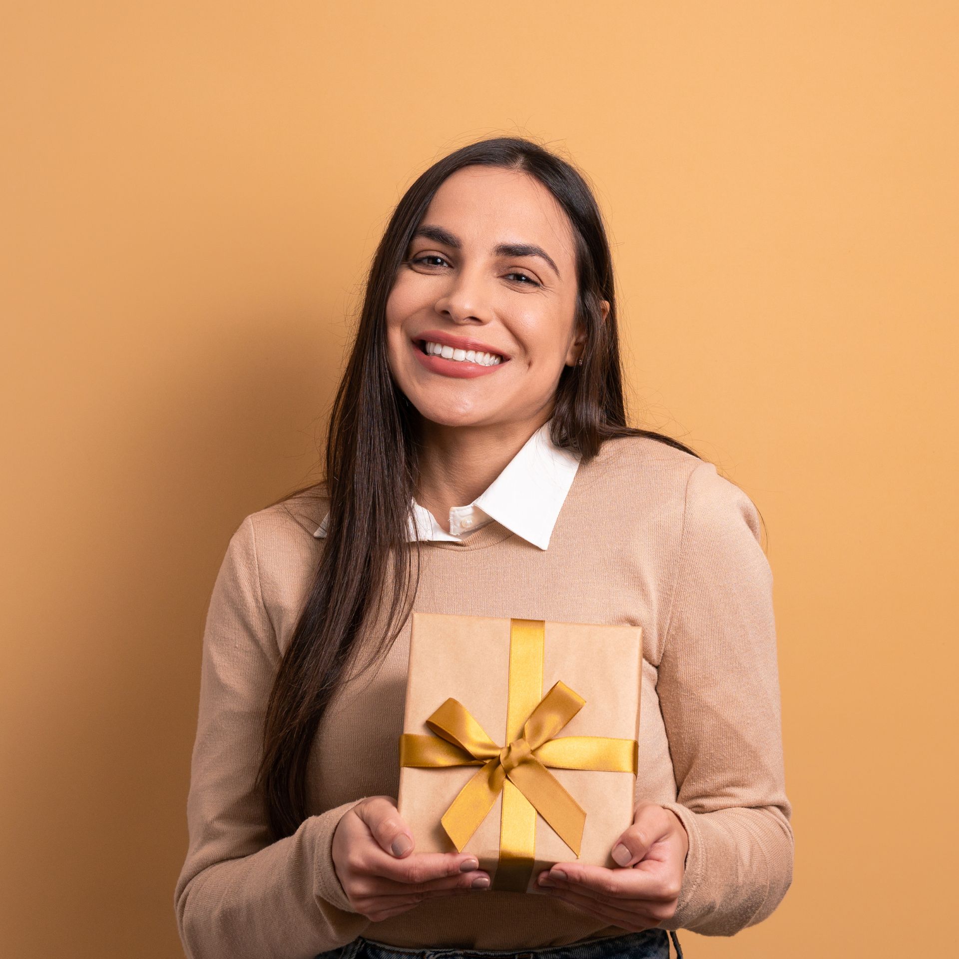 A woman is holding a gift box with a yellow ribbon and smiling.