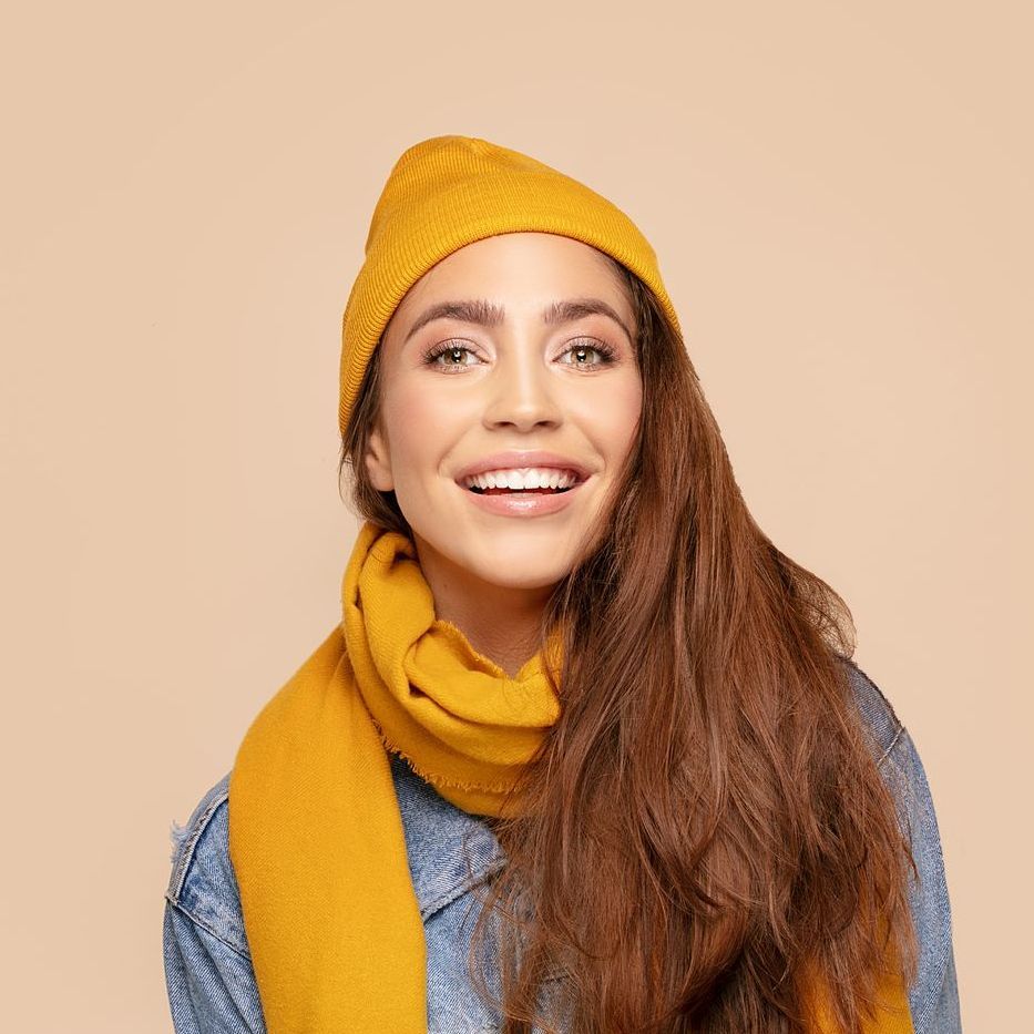 A woman wearing a yellow hat and scarf is smiling.