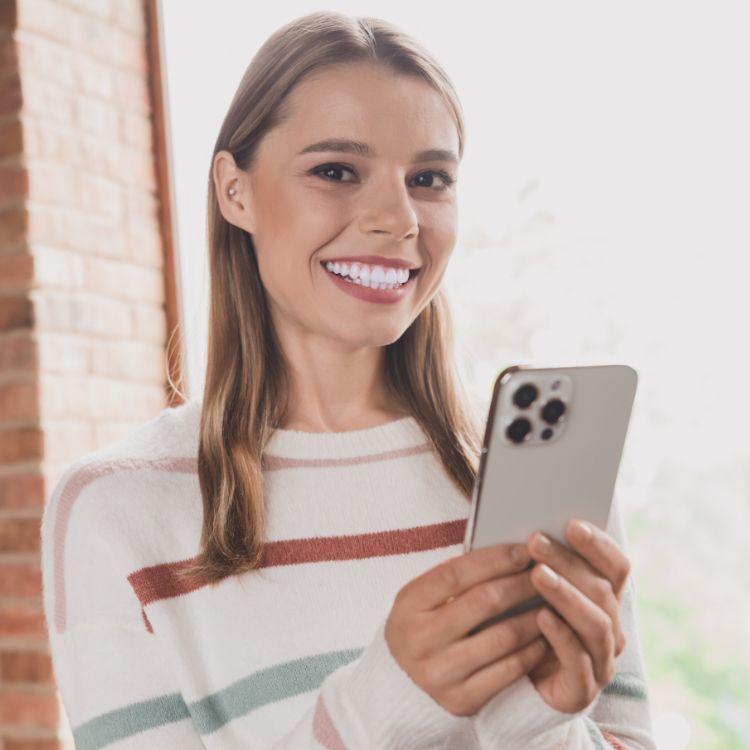 A woman is smiling while holding a cell phone