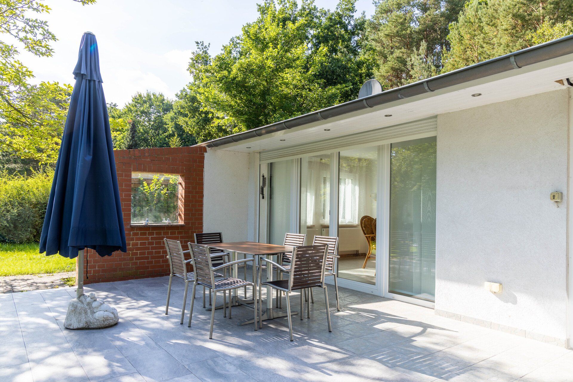 Eine Terrasse mit Tisch und Stühlen und einem Sonnenschirm vor einem Haus.