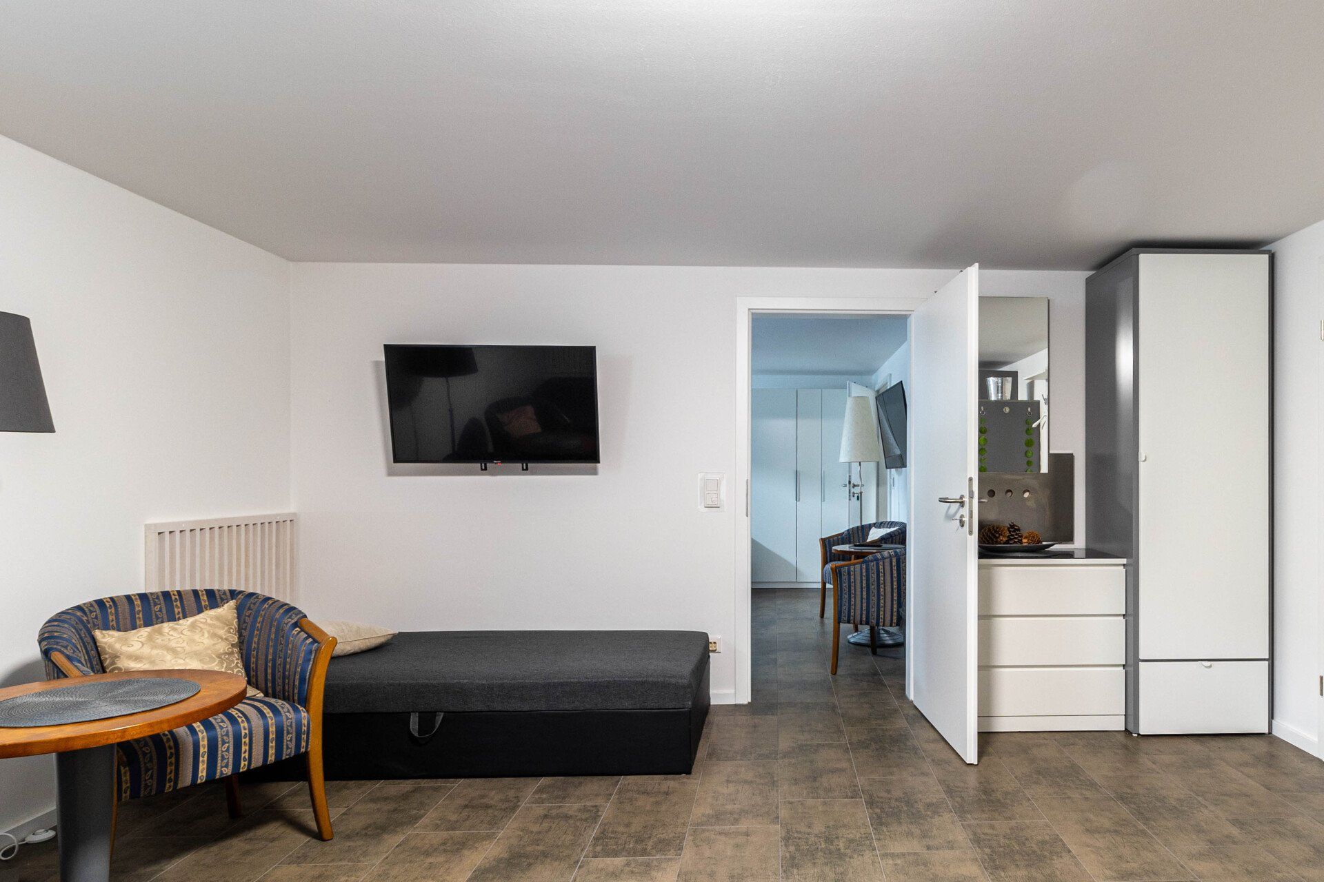 Ein Wohnzimmer mit Bett, Sessel, Tisch und Fernseher.