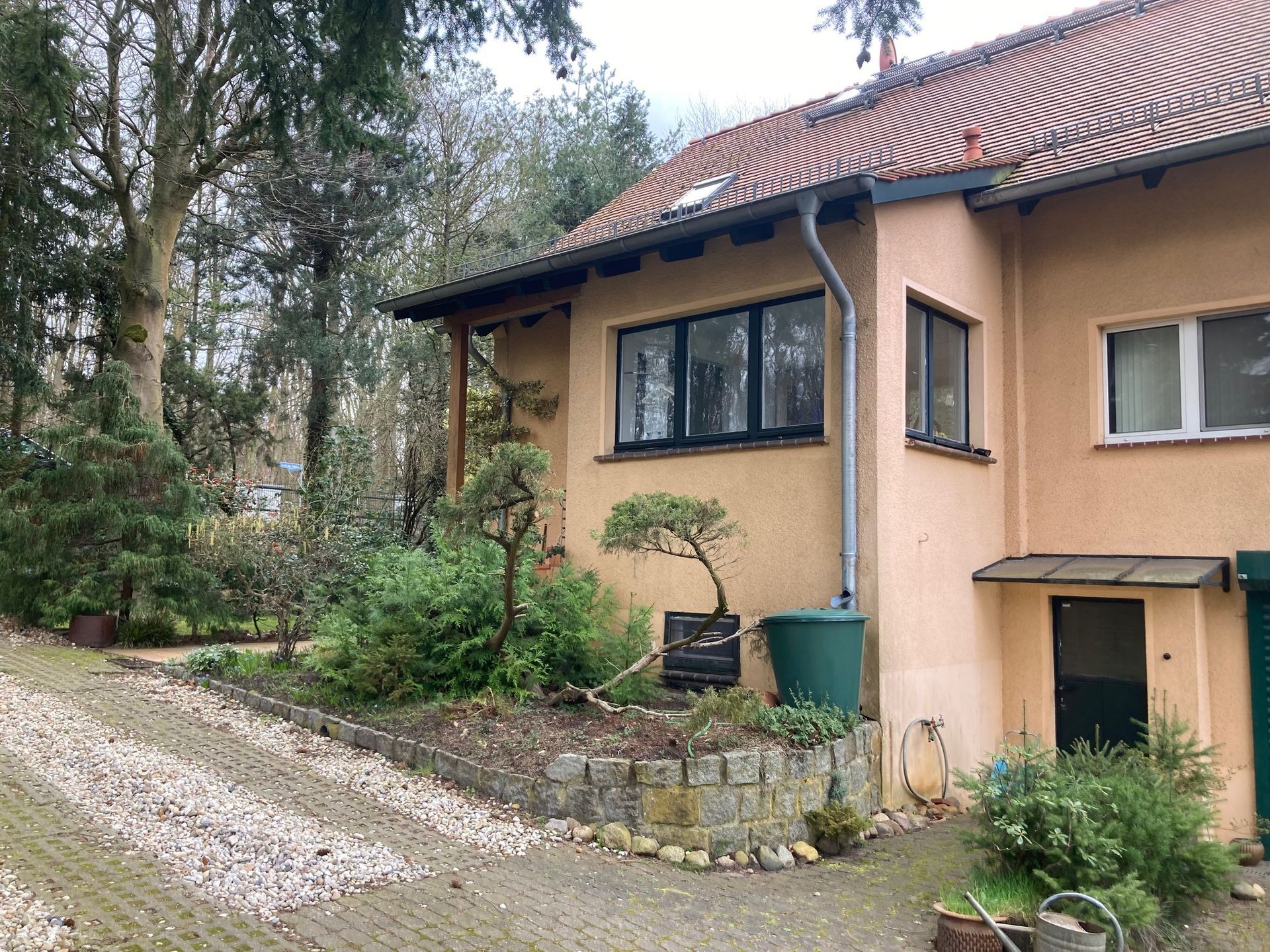 Ein Haus mit vielen Fenstern ist von Bäumen und Büschen umgeben.