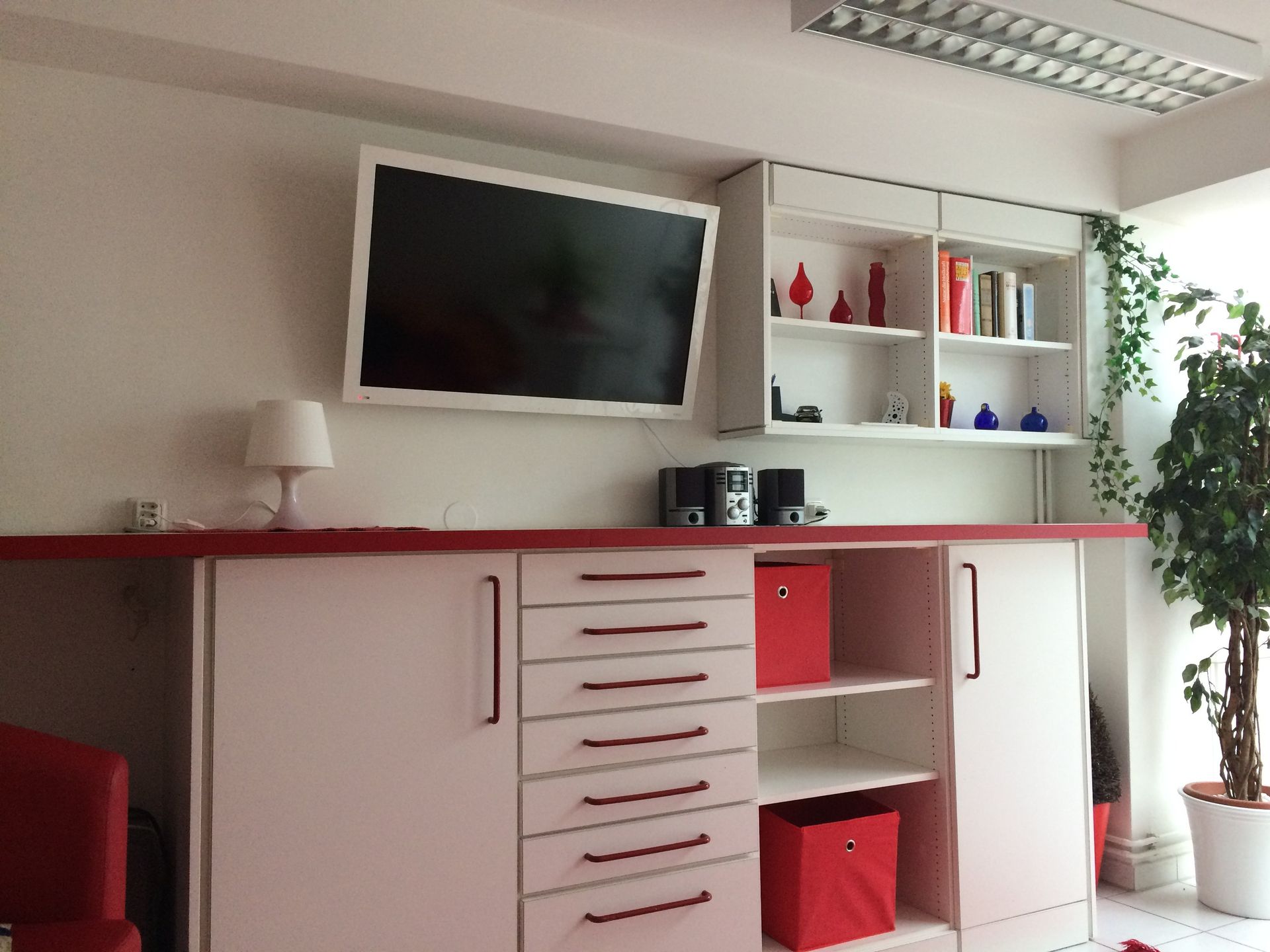 Ein Wohnzimmer mit weißen Schränken, roten Schubladen und einem Flachbildfernseher