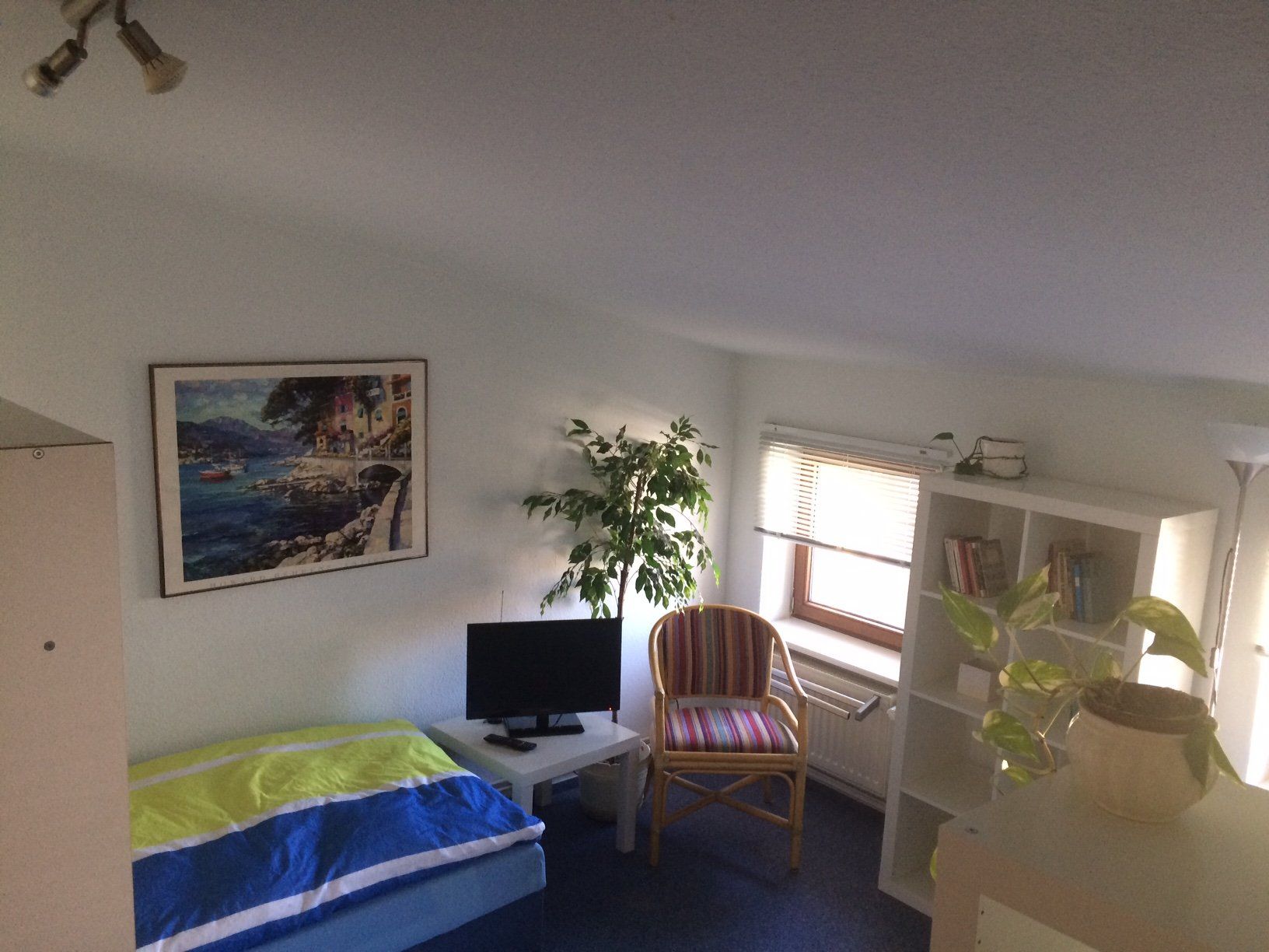 Ein Schlafzimmer mit Bett, Stuhl, Computer und einem Bild an der Wand.