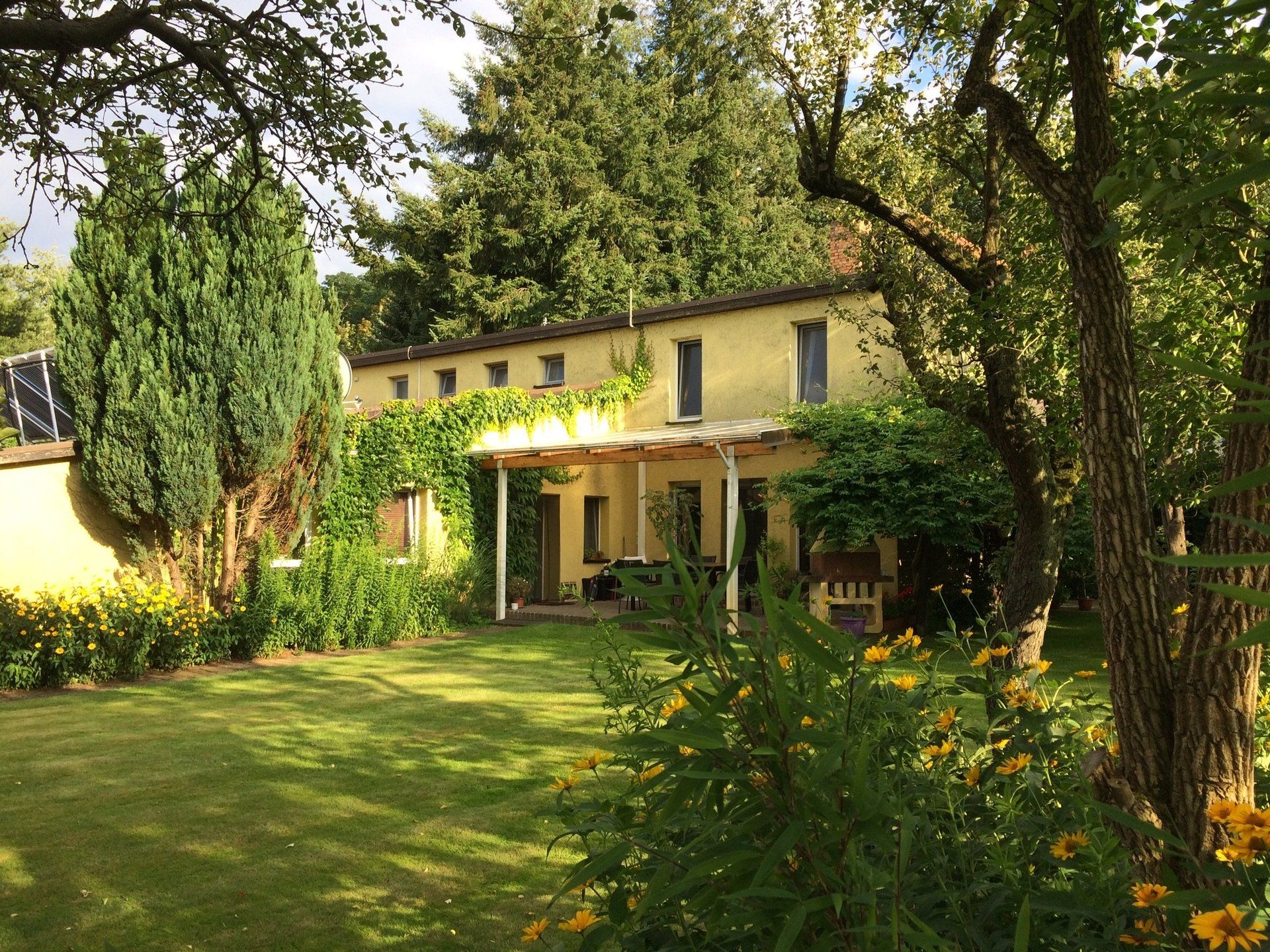 Ein gelbes Haus ist von Bäumen und Blumen umgeben