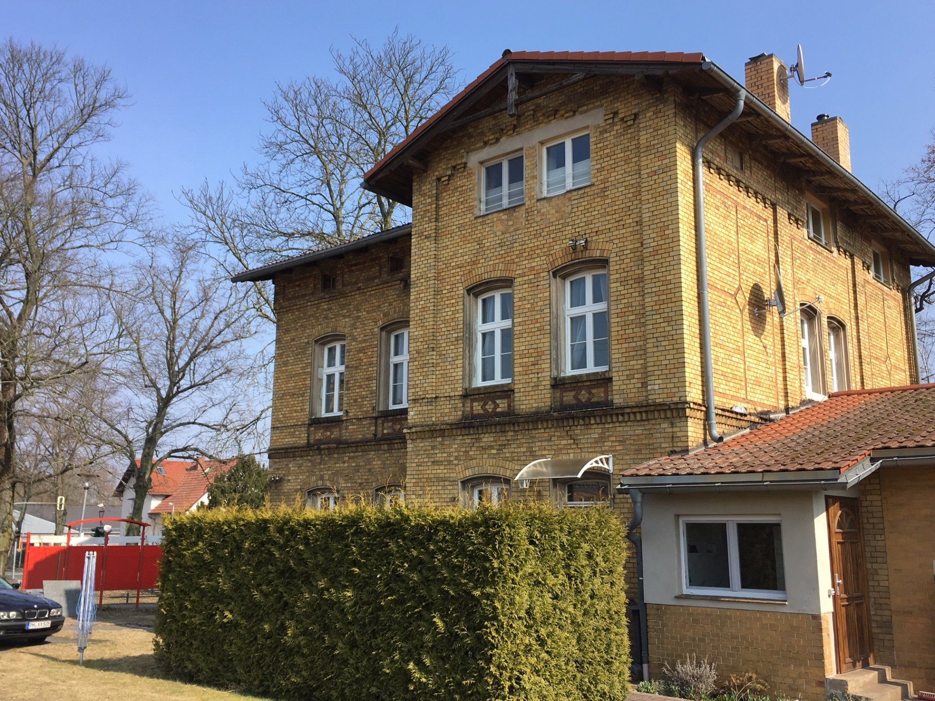 Ein großes gelbes Haus mit rotem Dach ist von Bäumen und Büschen umgeben.