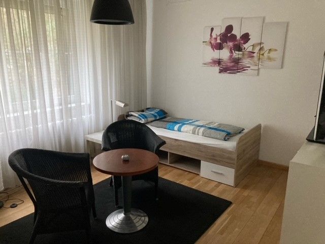 Ein Schlafzimmer mit einem Einzelbett, Stühlen, einem Tisch und einem Fernseher.