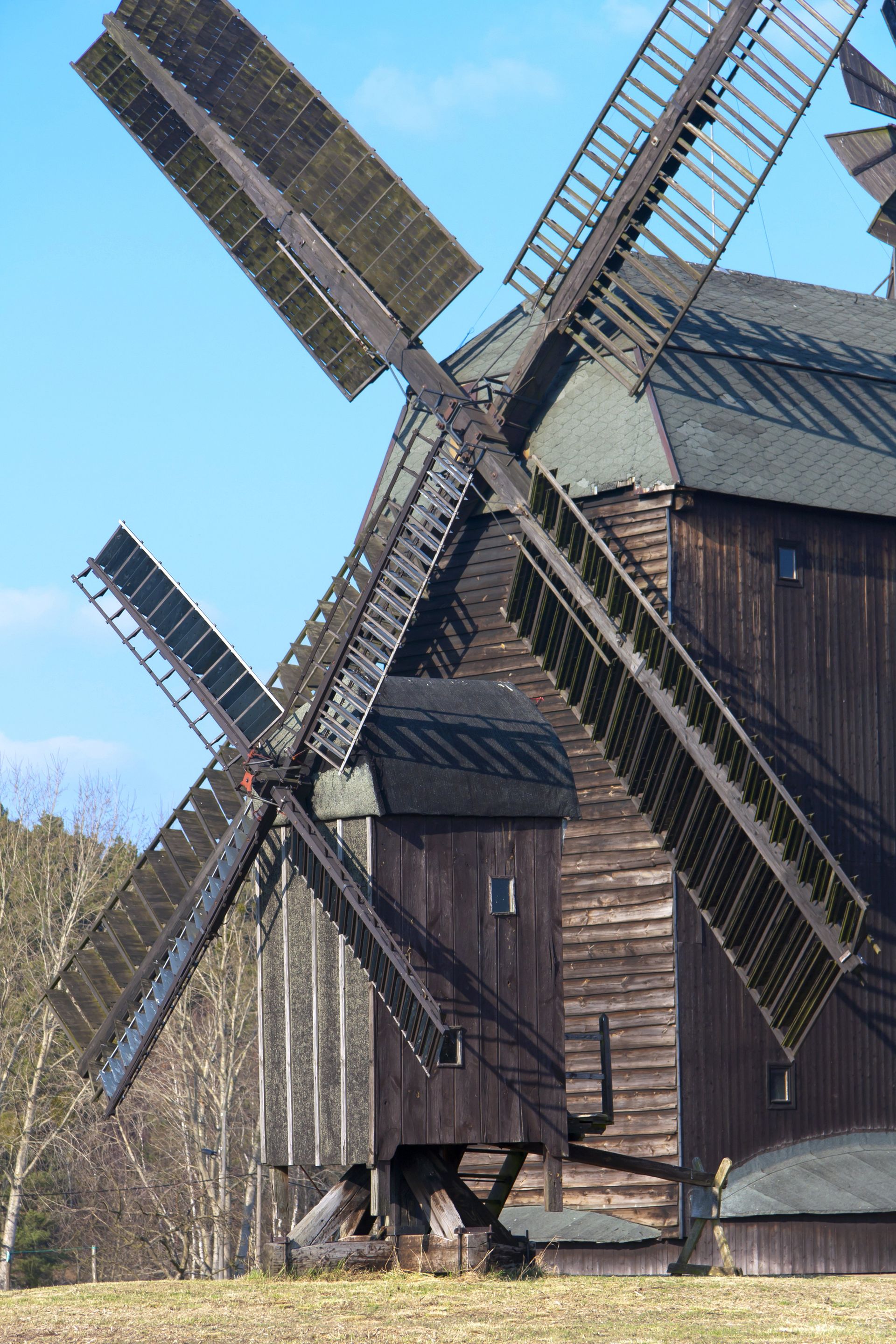 Eine hölzerne Windmühle steht vor einem Holzgebäude.
