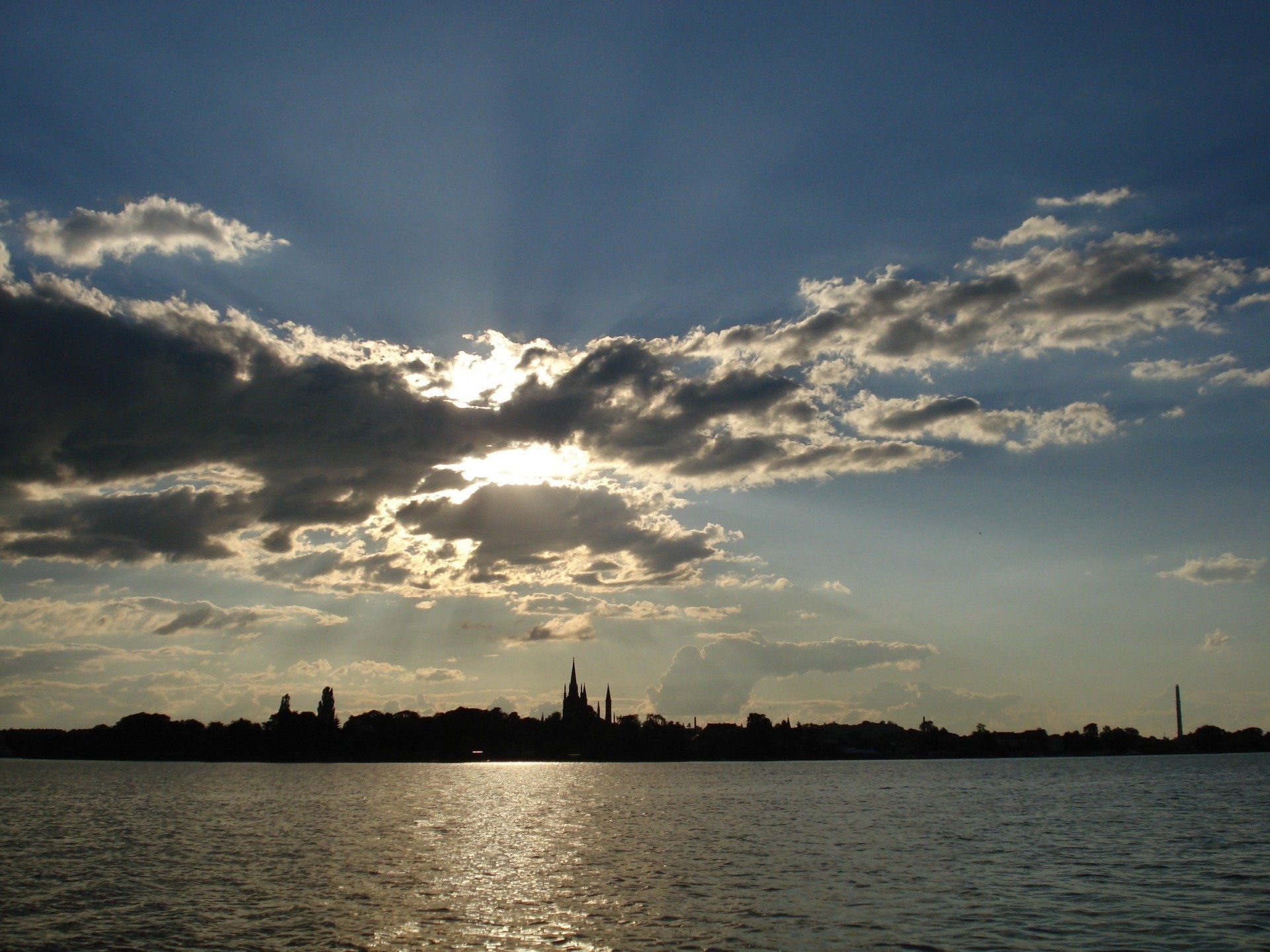 Die Sonne scheint durch die Wolken über einem Gewässer