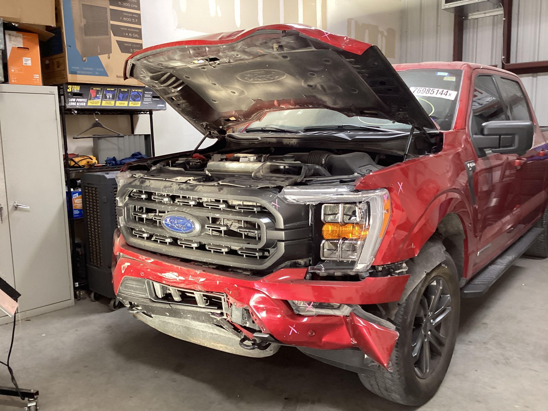 A red ford truck with its hood open is parked in a garage.