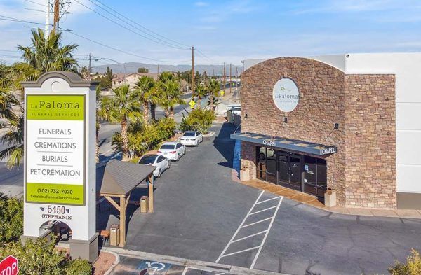 An exterior view of La Paloma Funeral Services, featuring a stone building, a tall signage post, and a parking lot.