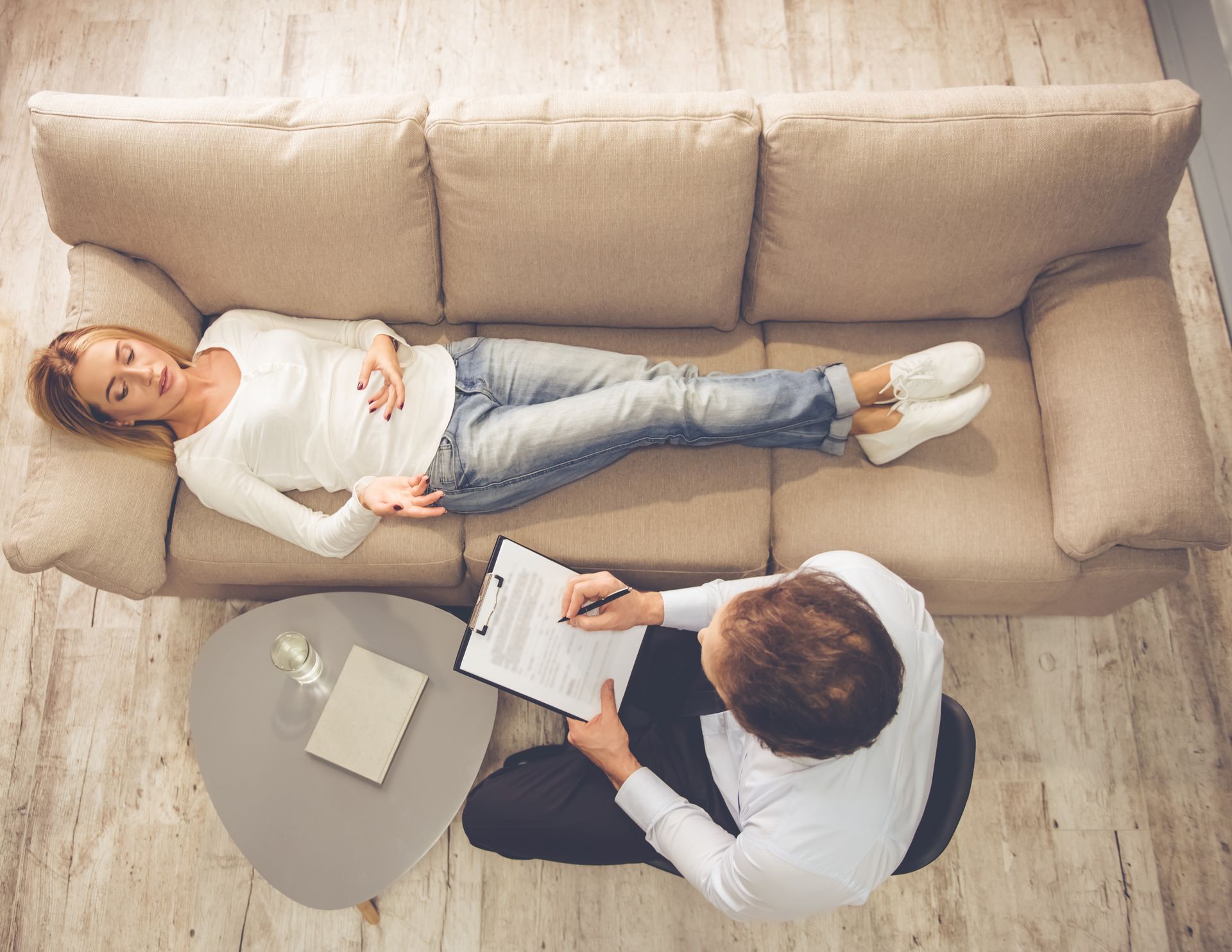 Therapist taking notes while client lies on a beige couch during a counseling session
