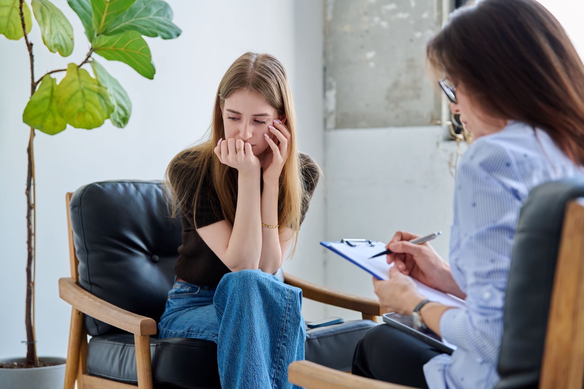 Therapist taking notes while a distressed client sits with hands over her face in a counseling office