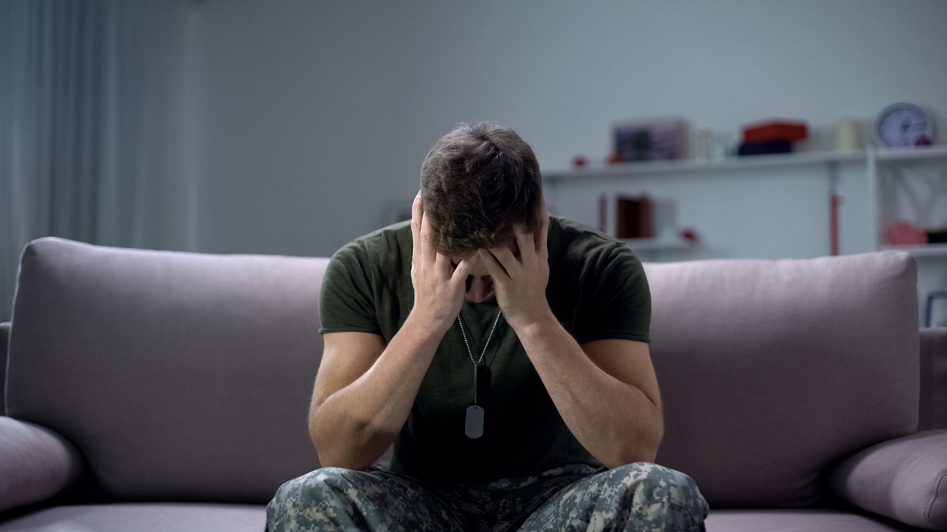 Person sitting on a couch, head in hands, appearing distressed in a dim living room.