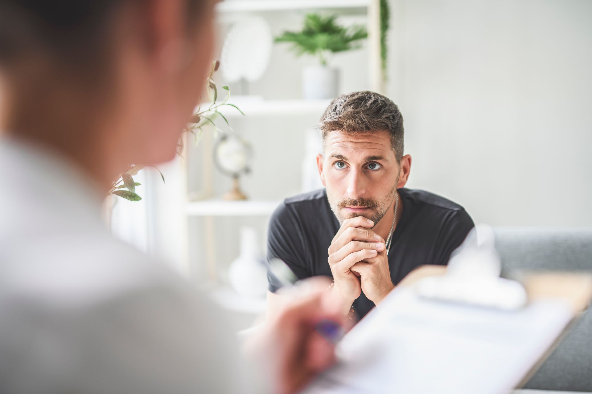 Man listening intently during a consultation, hands clasped, with a blurred person in foreground