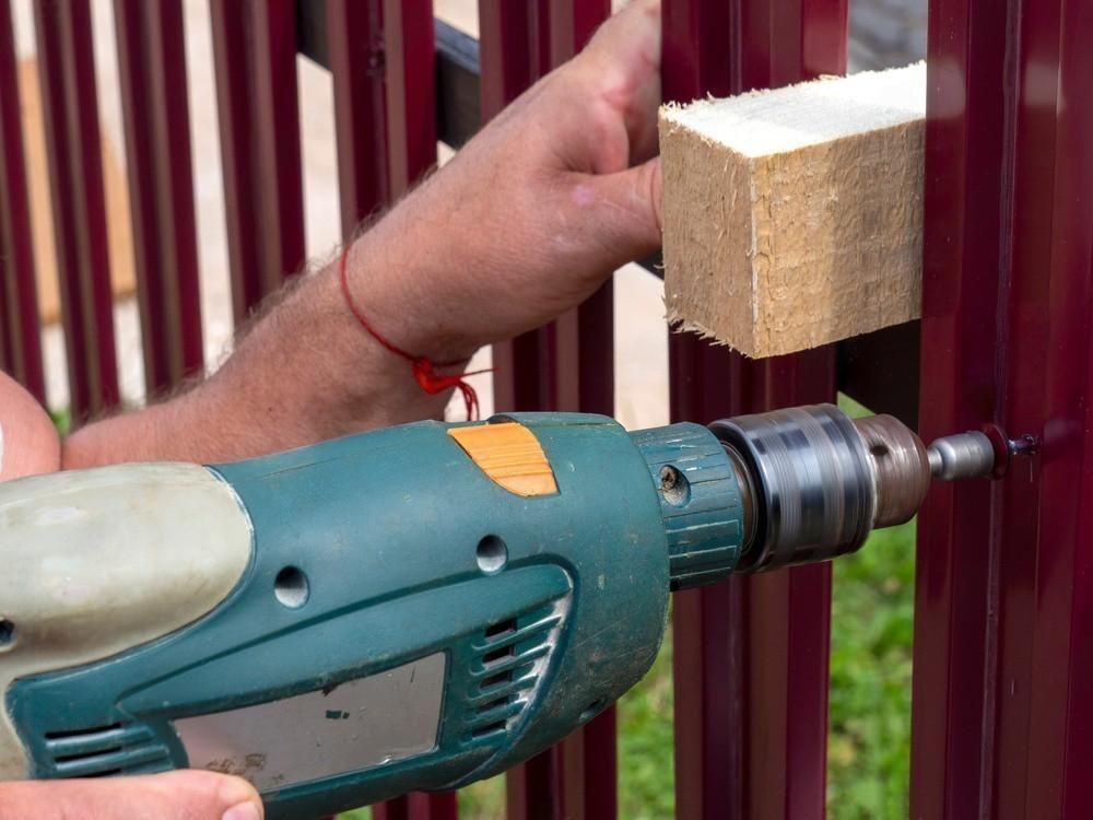 a man is using a drill to drill a hole in a fence .