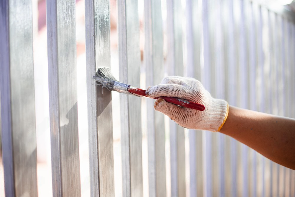 a person is painting a fence with a brush .