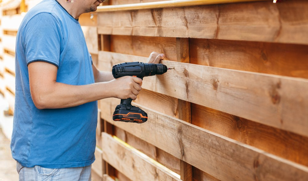 a man is using a drill to install a wooden fence .