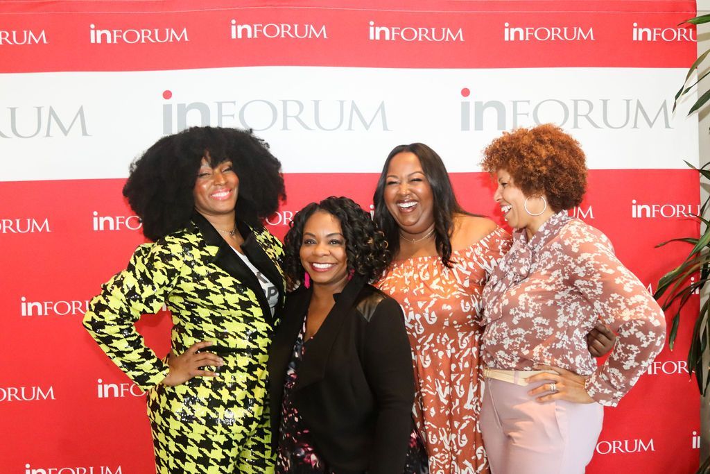 A group of women are posing for a picture in front of a red and white backdrop.