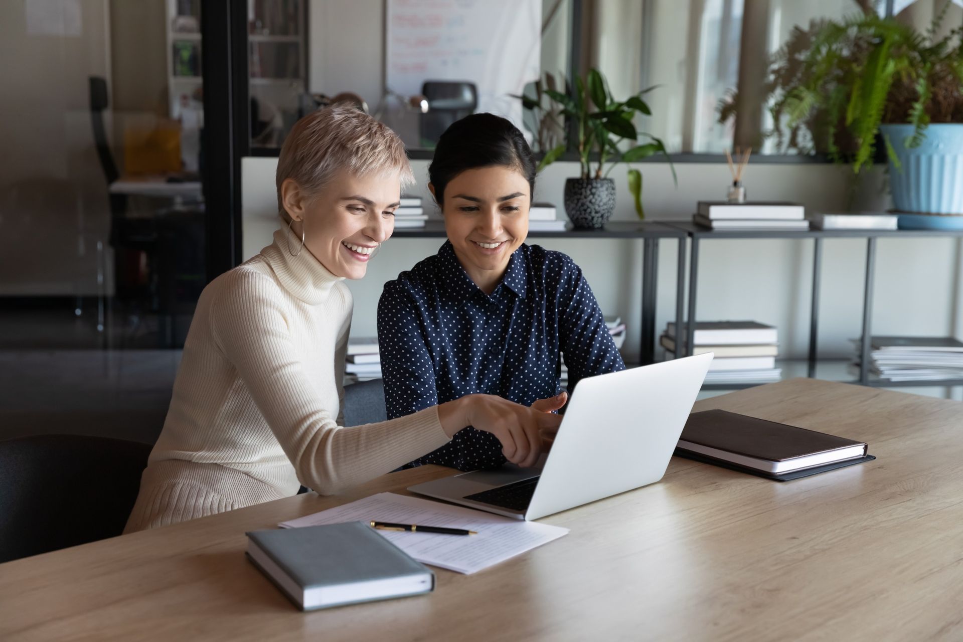 Two women are sitting at a table looking at a laptop computer.