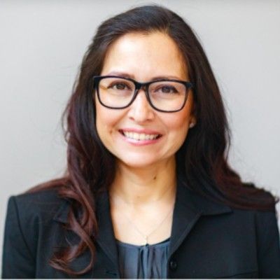 A woman wearing glasses and a black jacket is smiling.