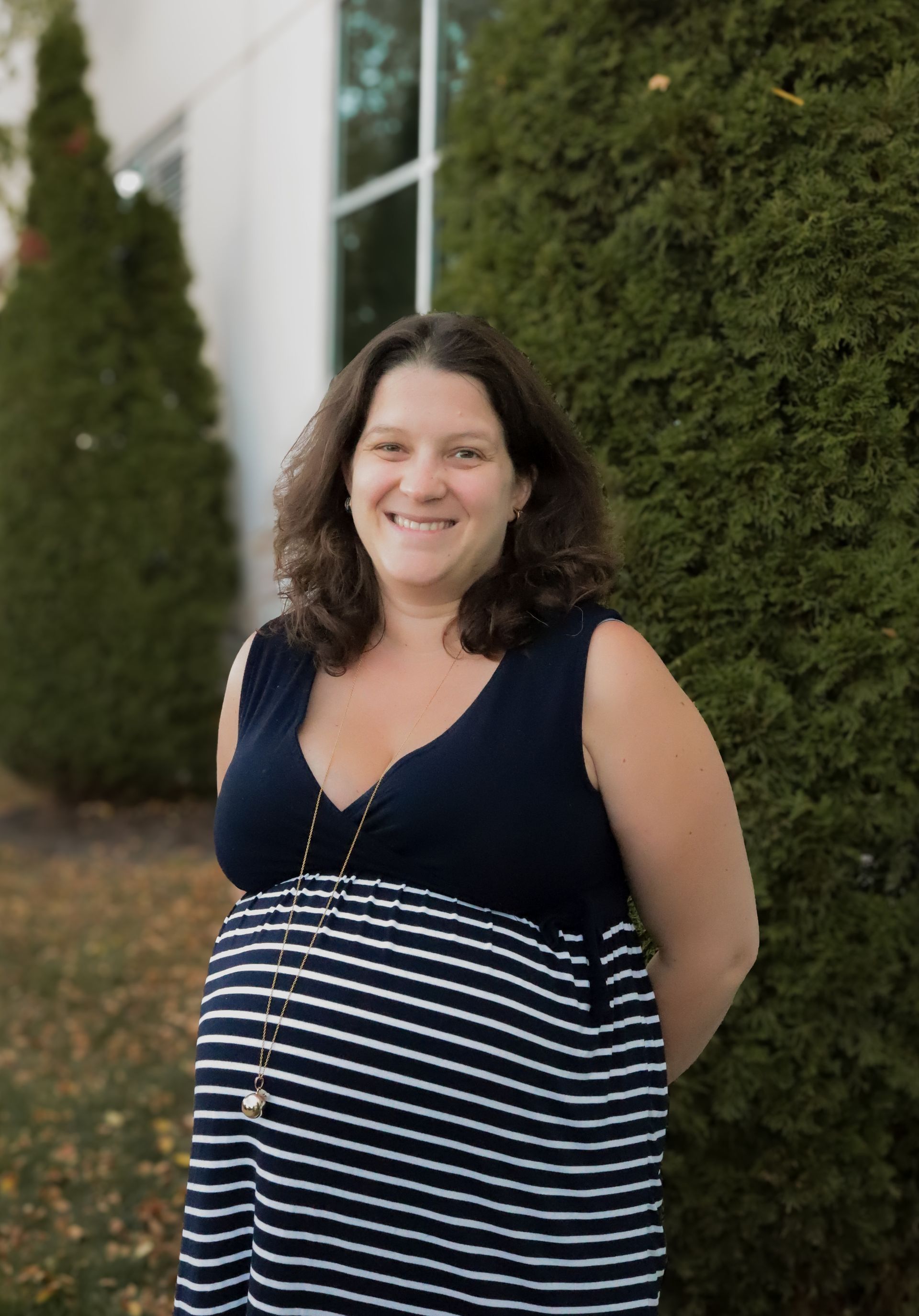 A woman in a striped dress is standing in front of a building and smiling.