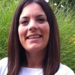 A woman with long dark hair is smiling in front of a bush.