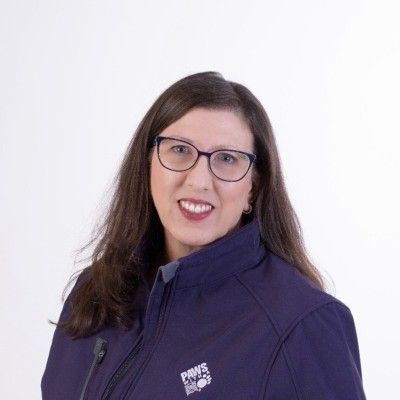 A woman wearing glasses and a purple jacket is smiling for the camera.