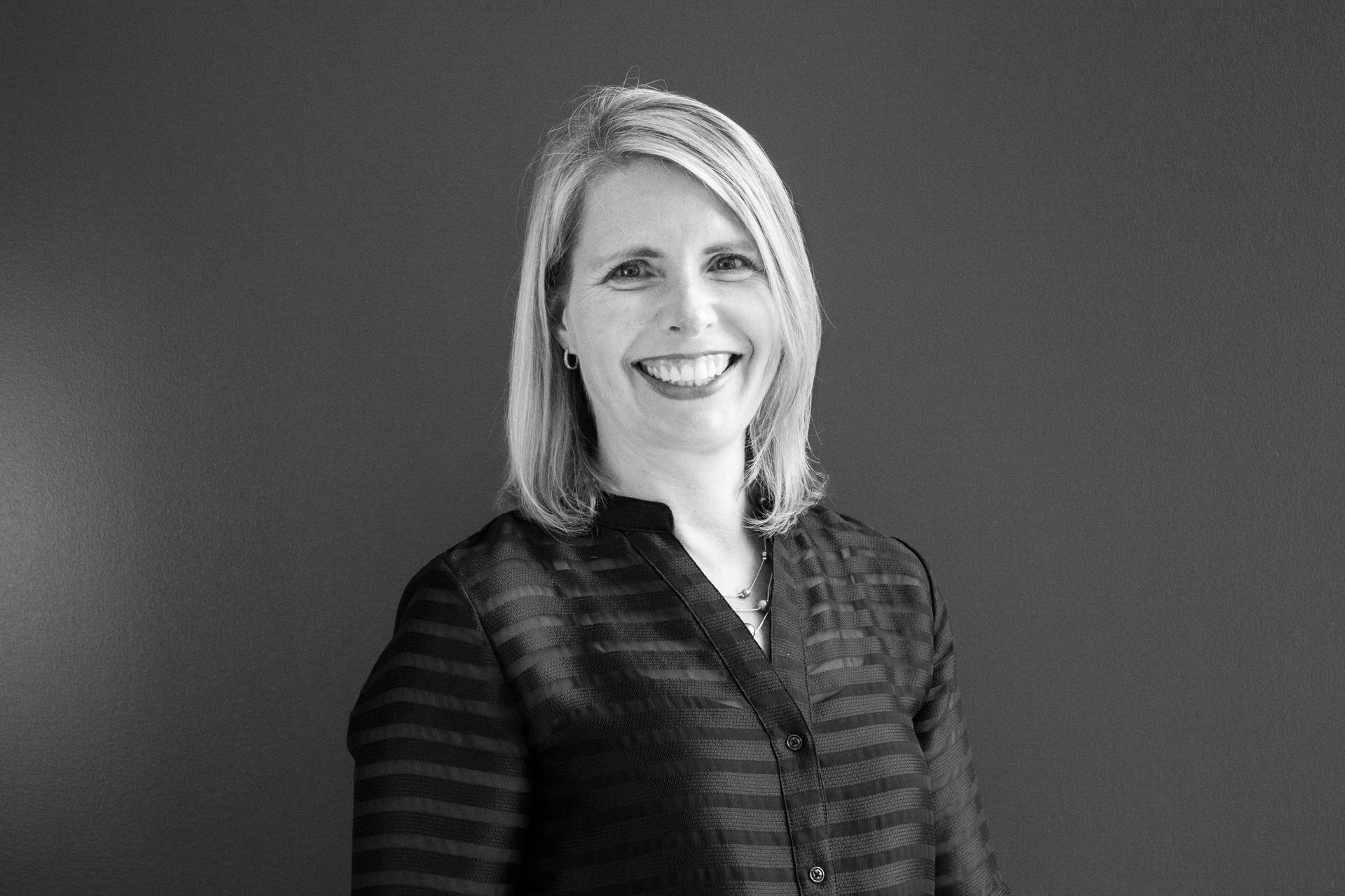 A woman in a striped shirt is smiling in a black and white photo.
