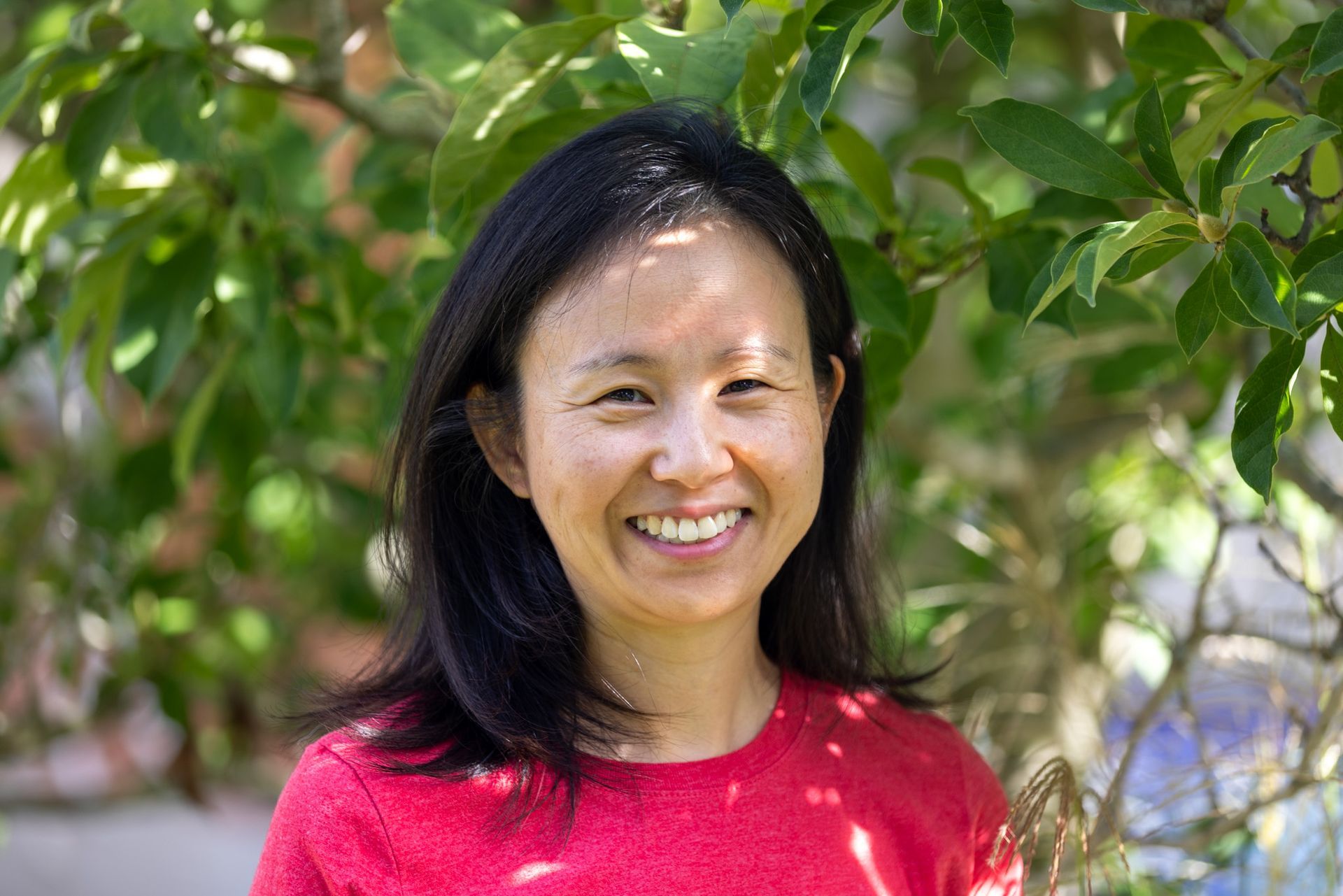 A woman in a red sweater is smiling in front of a tree.