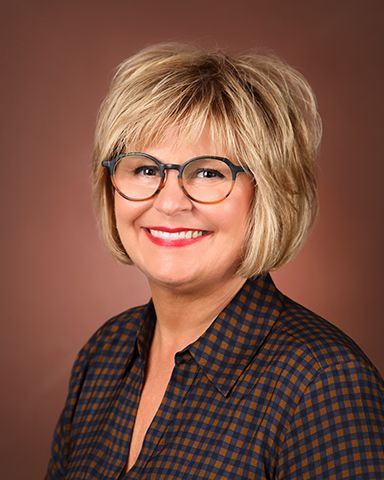 A woman wearing glasses and a plaid shirt is smiling for the camera.