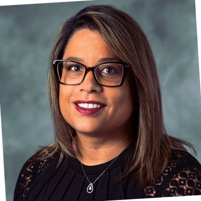 A woman wearing glasses and a necklace is smiling for the camera.