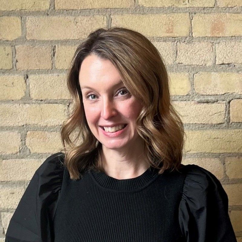 A woman in a black sweater is smiling in front of a brick wall.