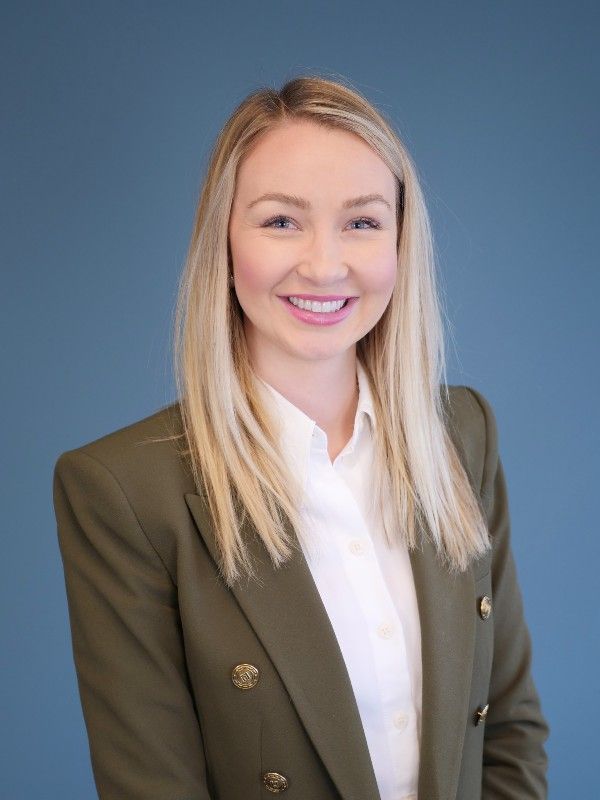 A woman in a green jacket and white shirt is smiling for the camera.