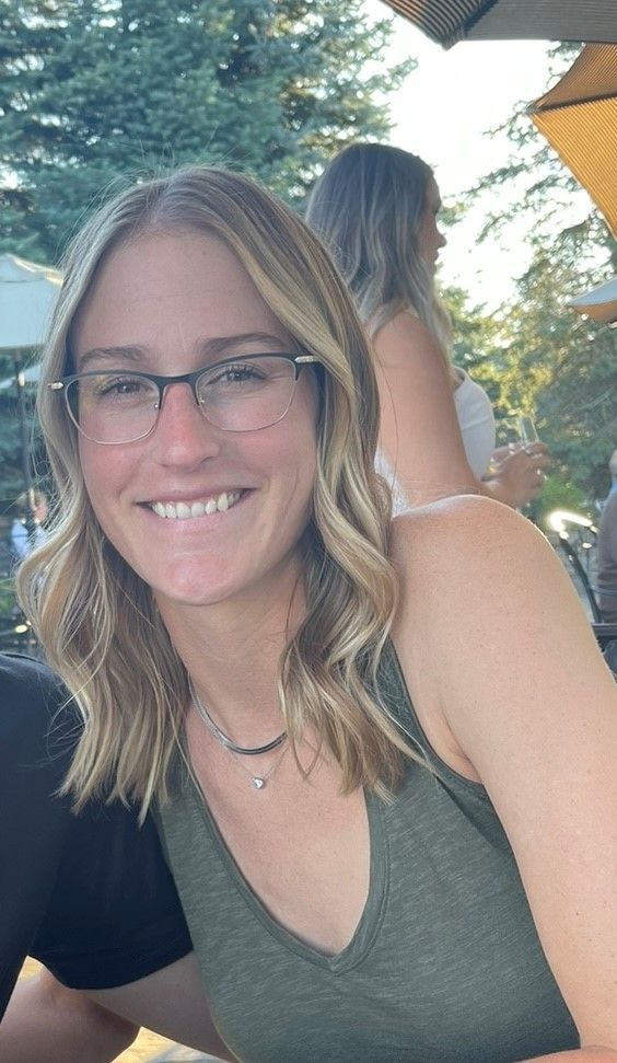 A woman wearing glasses and a green tank top is smiling for the camera.