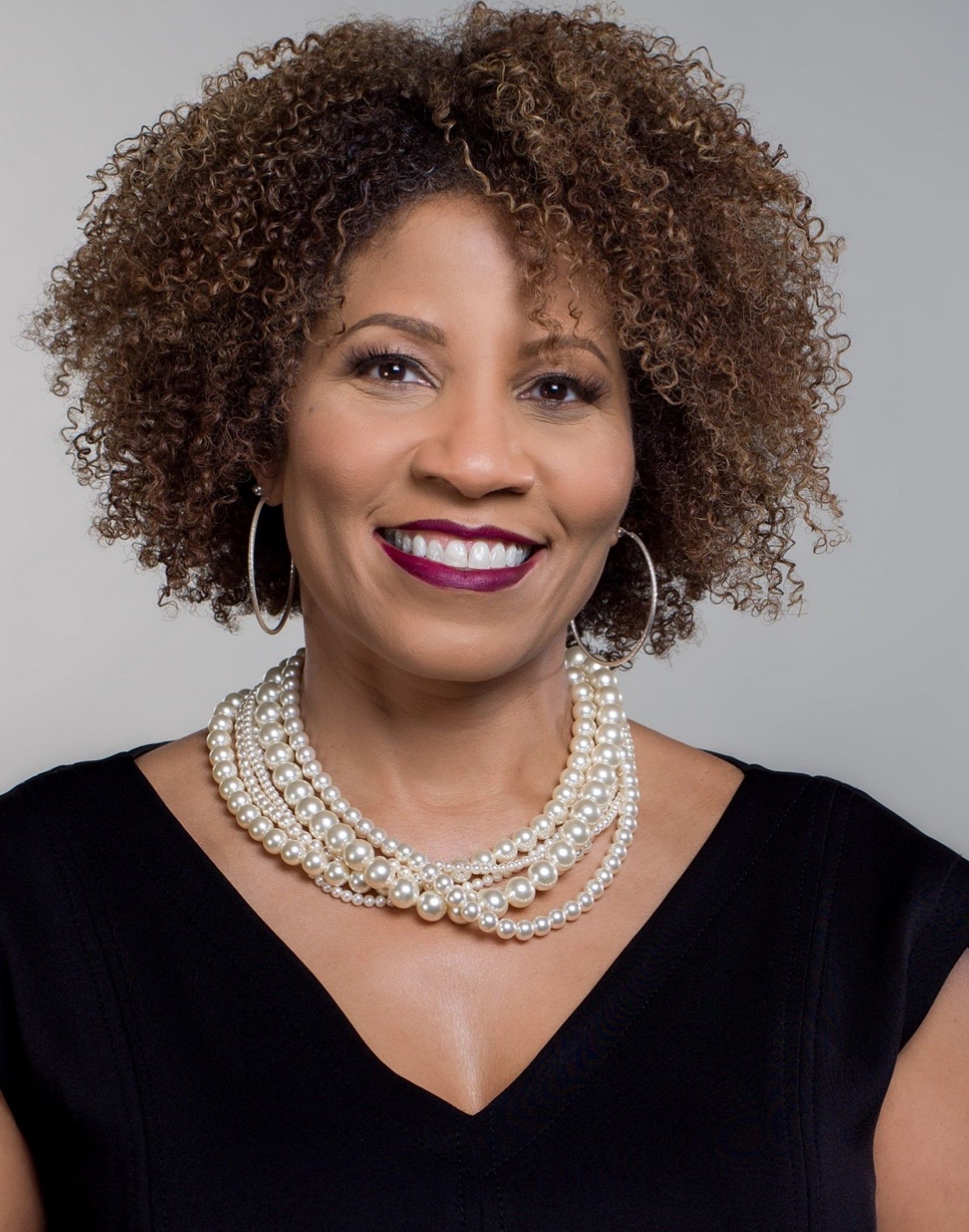 A woman with curly hair is wearing a pearl necklace and earrings.