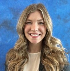 A woman with long blonde hair is smiling in front of a blue background.