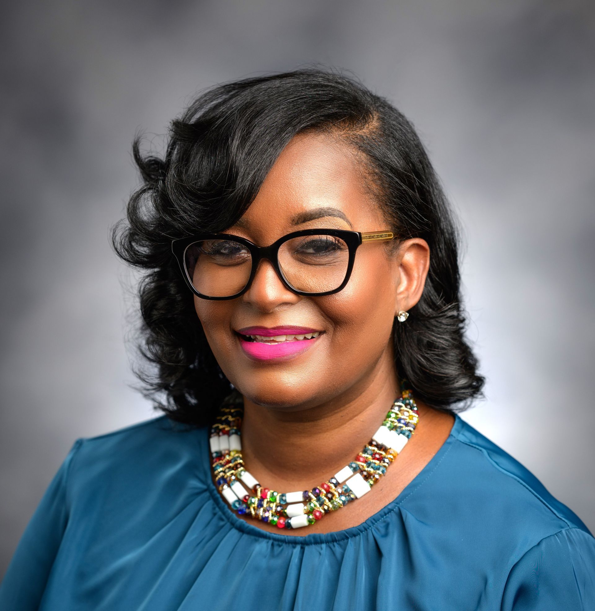 A woman wearing glasses and a necklace is smiling for the camera.